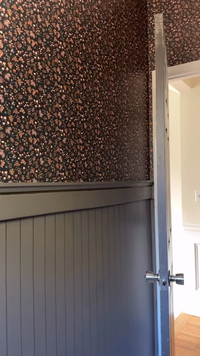 A grey beadboard door with a silver handle stands against patterned wallpaper.