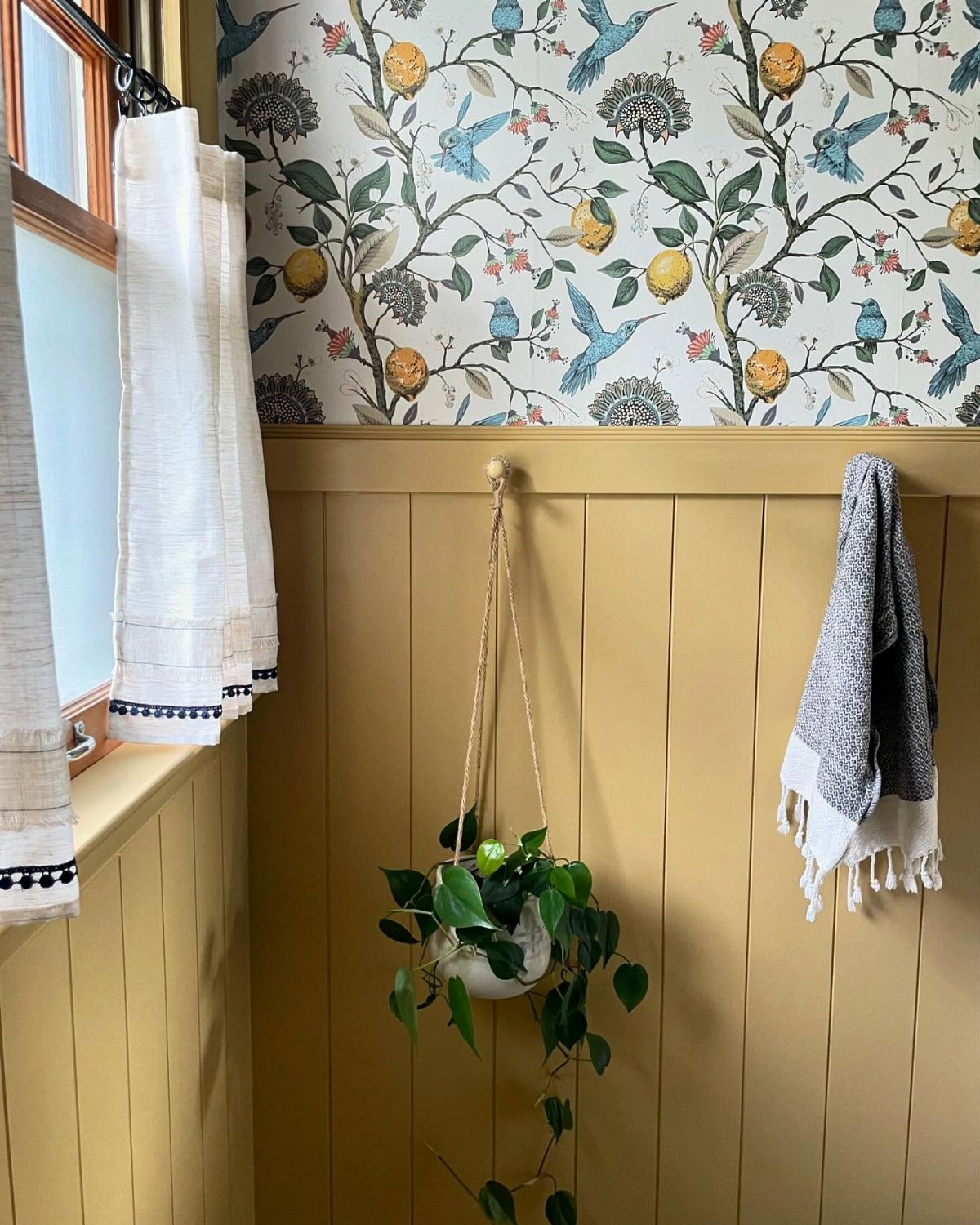 Yellow beadboard paneling on a bathroom wall below floral bird and lemon wallpaper.