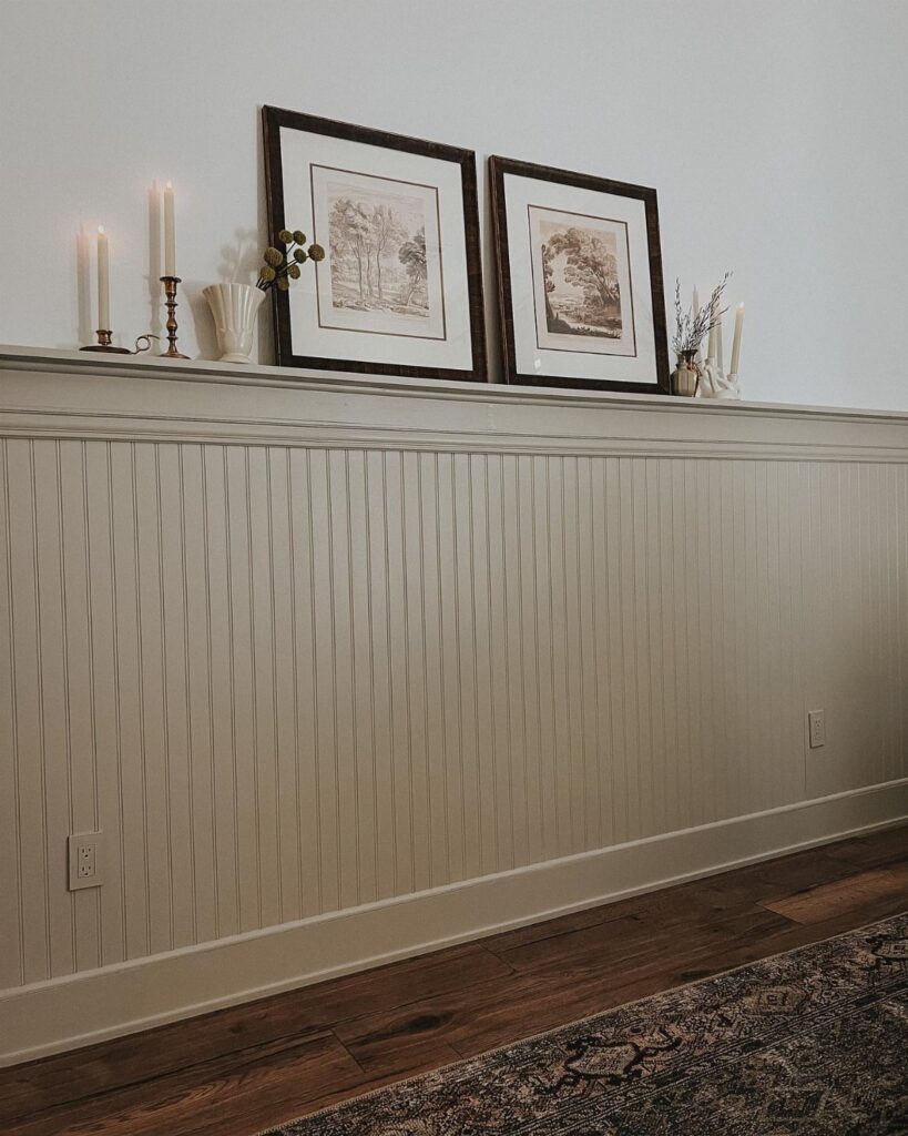 Cream beadboard wainscoting on a white wall with framed art and candles on a ledge.