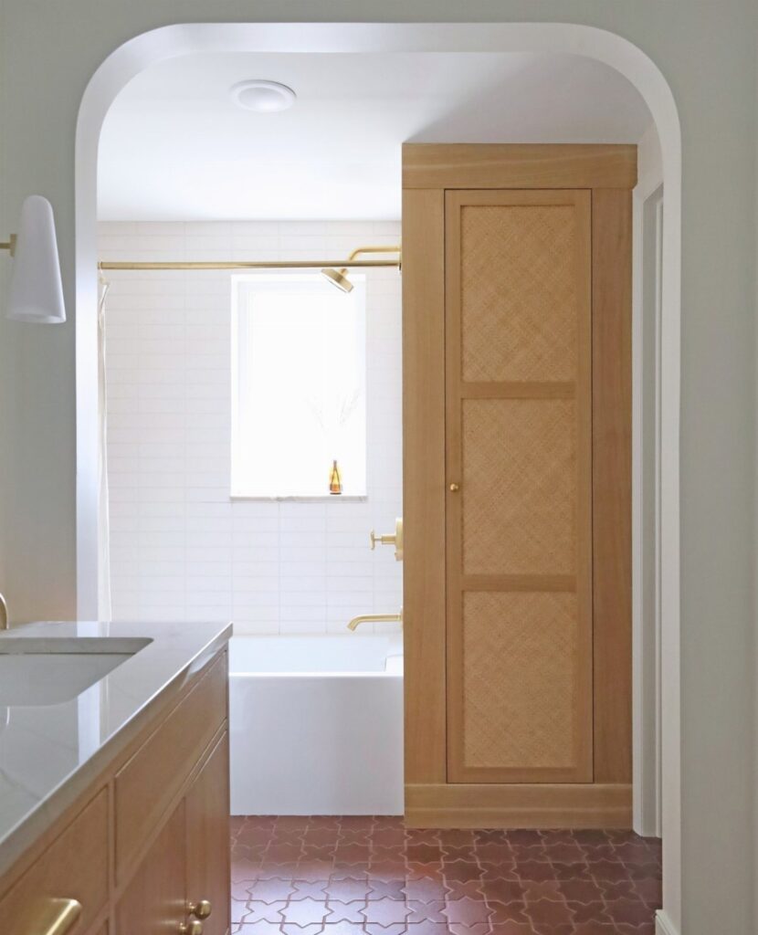 Reddish-brown patterned ceramic tiles on a bathroom floor near a white bathtub and wooden cabinets.