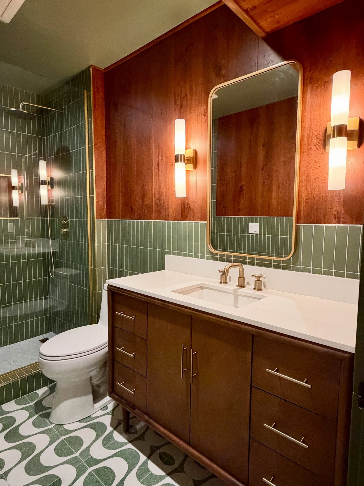 A modern bathroom with a wooden vanity, green tiles, and patterned floor tiles.