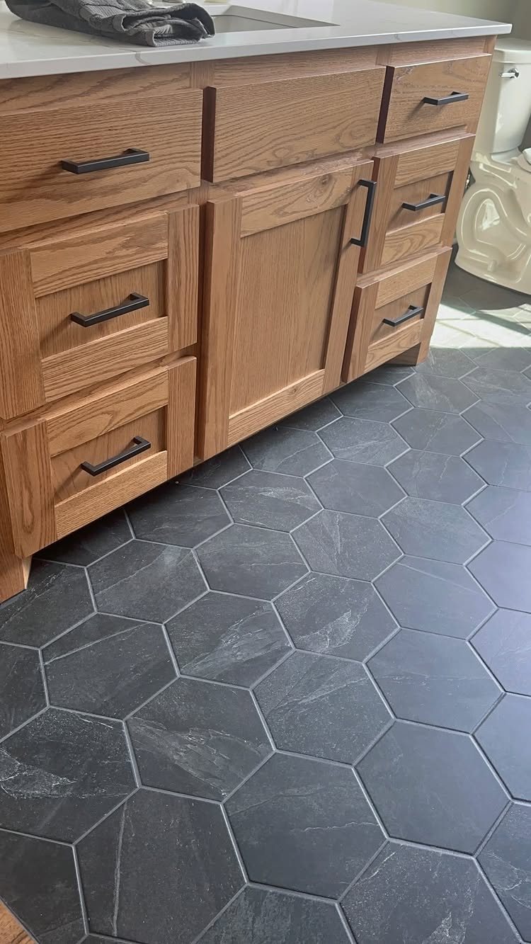 Dark grey hexagonal tiles on a bathroom floor next to a wooden vanity.