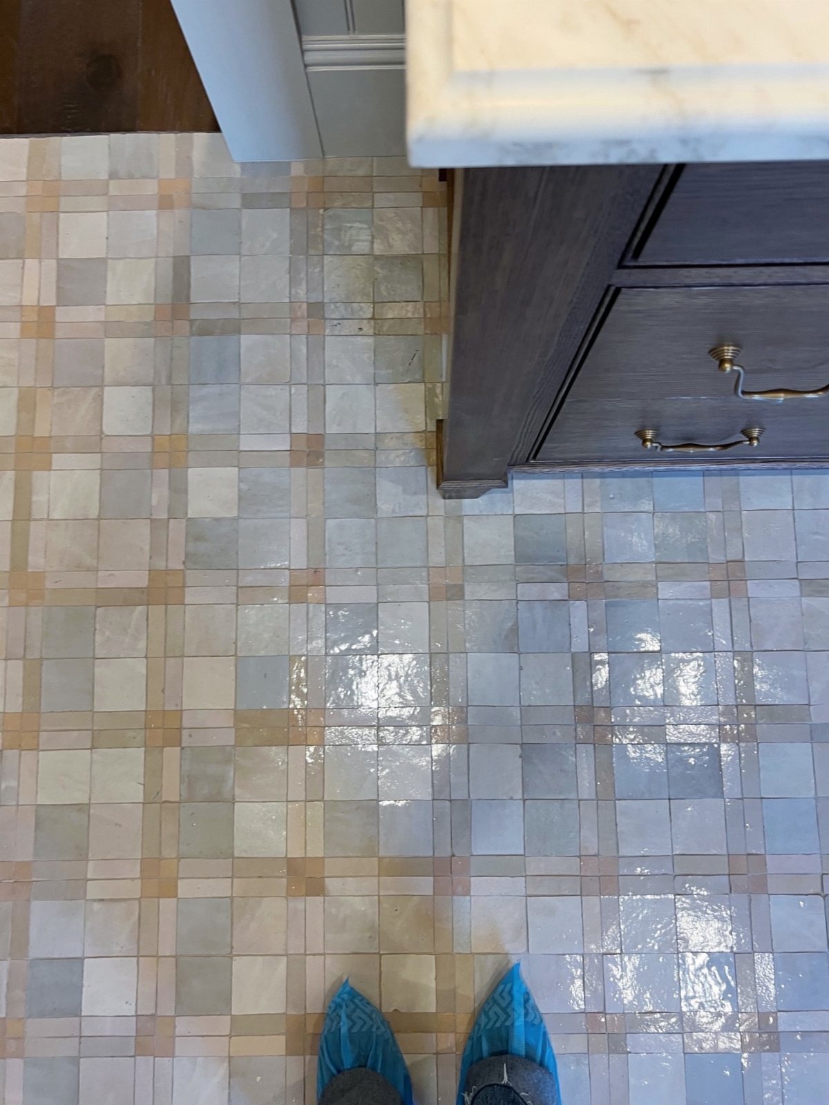 Glossy square tiles in shades of blue and tan covering a bathroom floor near a dark vanity.