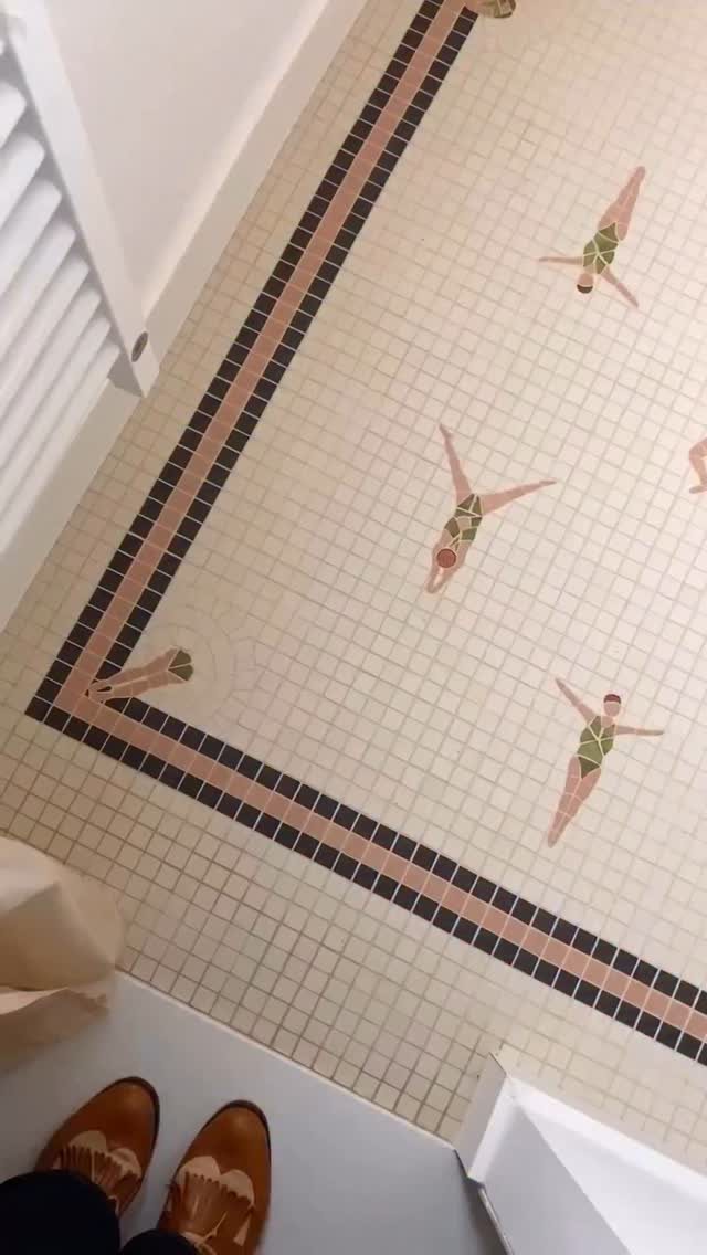 Small mosaic tiles on a bathroom floor featuring decorative borders and swimming figure patterns.
