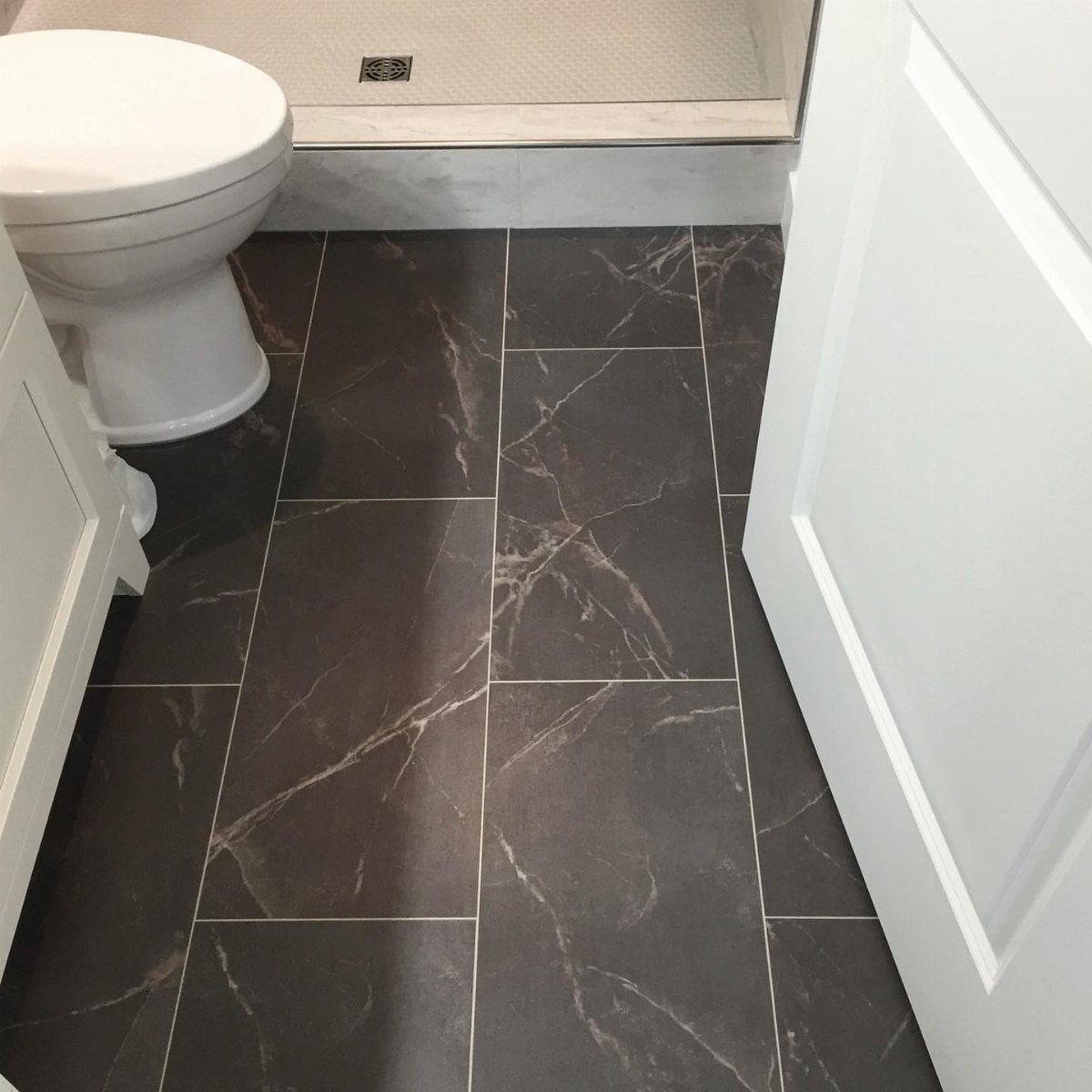 Dark grey marble-patterned tiles covering a bathroom floor next to a white toilet.