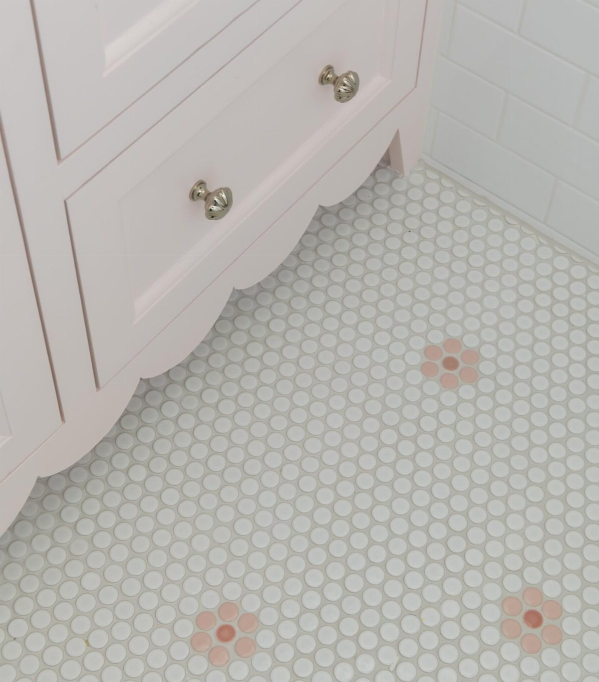 White penny tile bathroom floor decorated with small pink ceramic blossom patterns near a pink vanity.