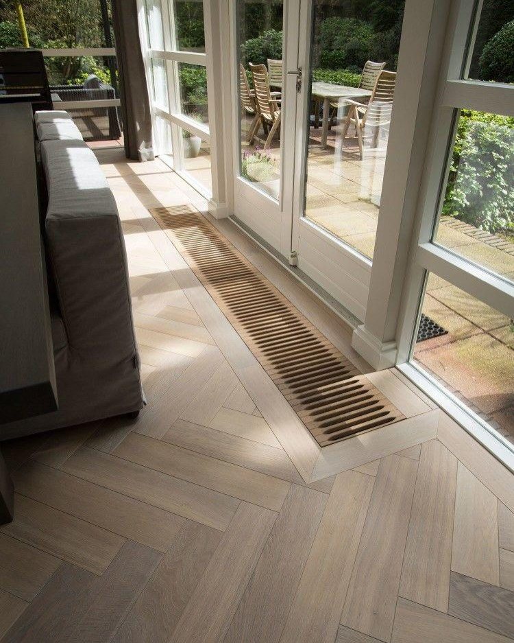 Light wood flooring with a herringbone pattern in a bright sunlit room near glass doors.
