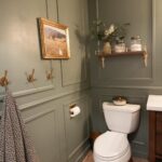 Sage green wainscoting paneling installed on the lower half of a bathroom wall near a white toilet.