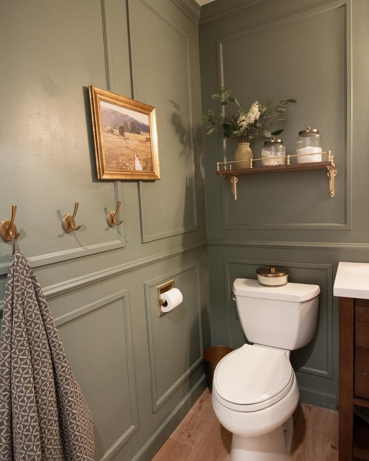 Sage green wainscoting paneling installed on the lower half of a bathroom wall near a white toilet.