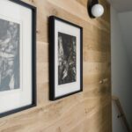 Natural wood shiplap wall decorated with black framed art and a white globe light fixture.