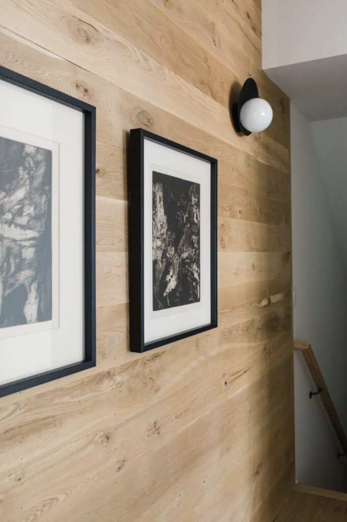 Natural wood shiplap wall decorated with black framed art and a white globe light fixture.