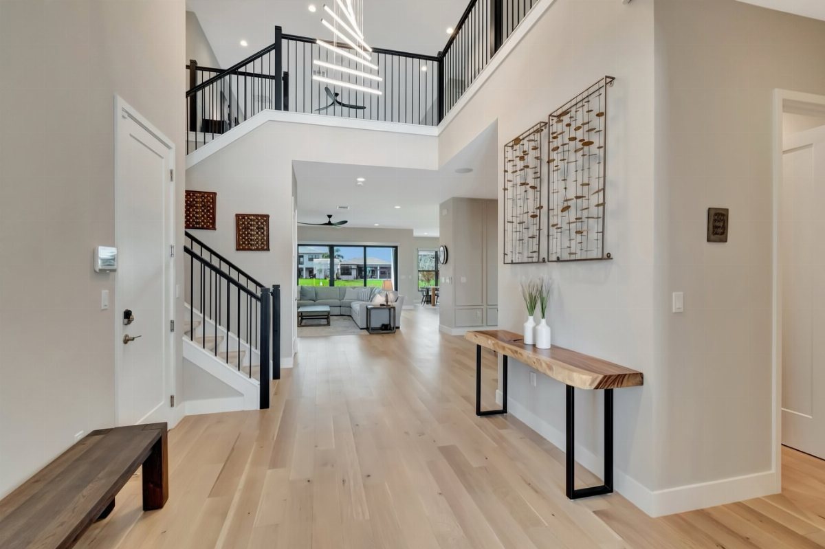 Light-colored wide plank hardwood flooring extends through a bright, modern home hallway and living area.