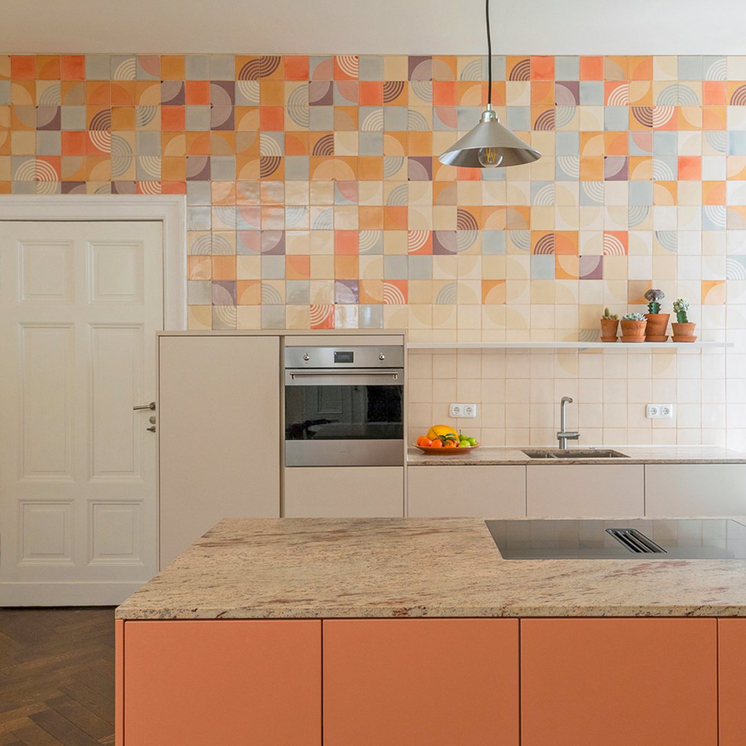 Patterned kitchen tiles in orange and blue geometric designs covering the wall above white cabinets.