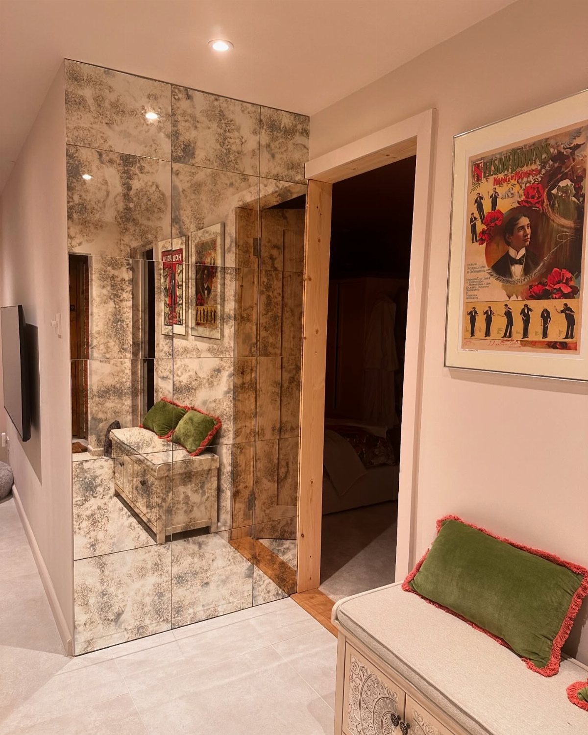 Antiqued mirror tiles covering a wall in a room with a bench and framed art.