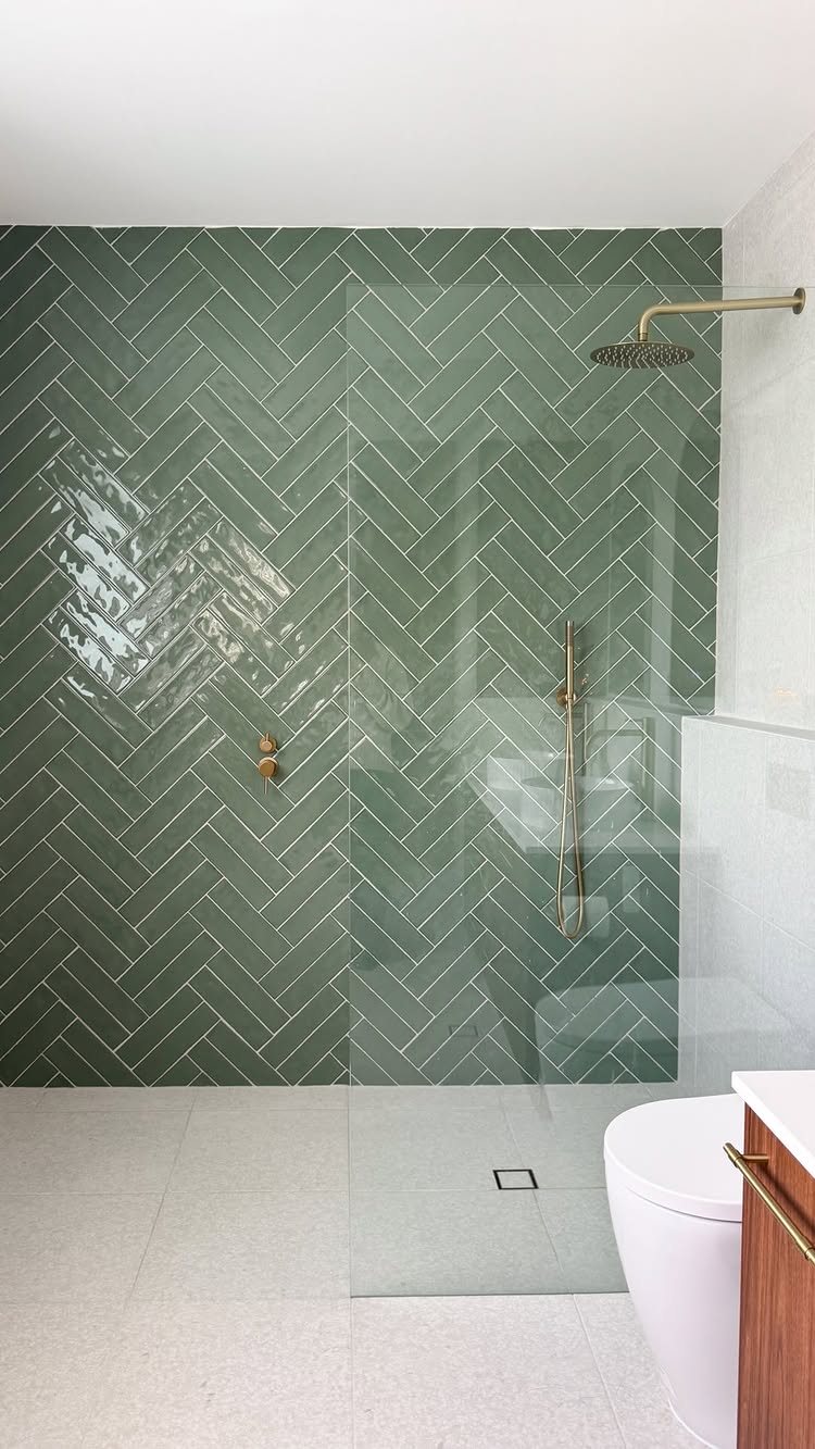Green herringbone patterned tiles covering a bathroom accent wall behind a glass shower door.