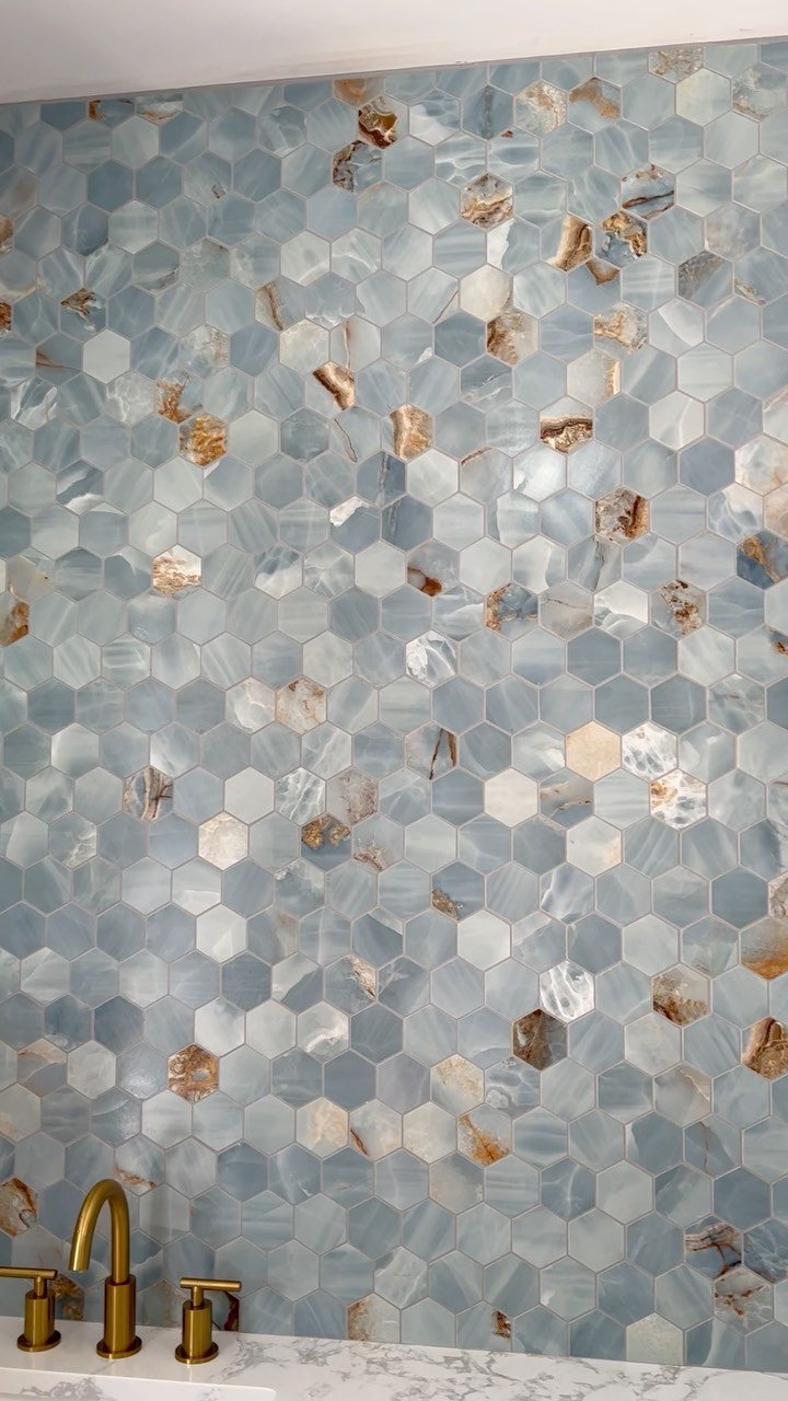 Hexagonal blue and brown patterned tiles covering a bathroom wall behind a gold faucet.