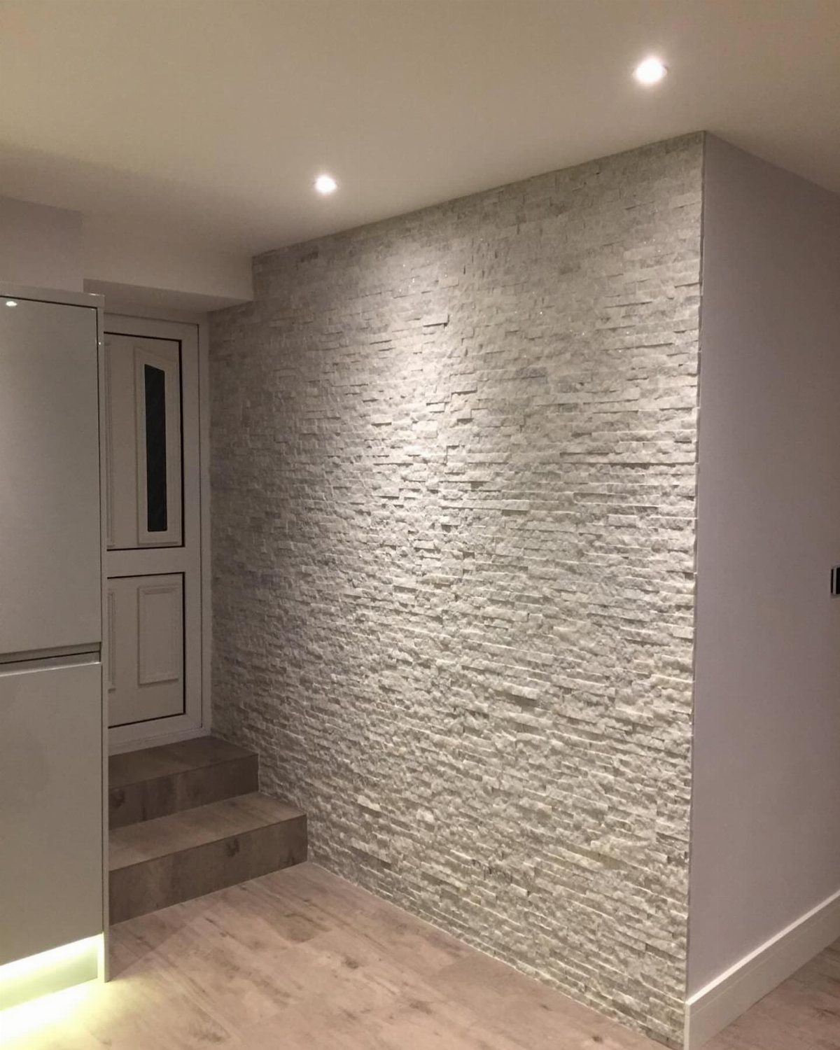Textured white split face stone feature wall illuminated by warm recessed ceiling lights.