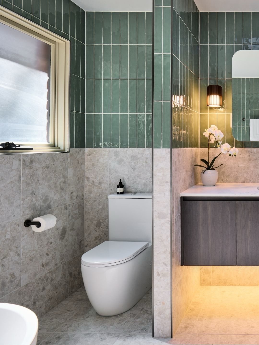 Green vertical subway tiles and grey stone tiles in a modern bathroom setting.