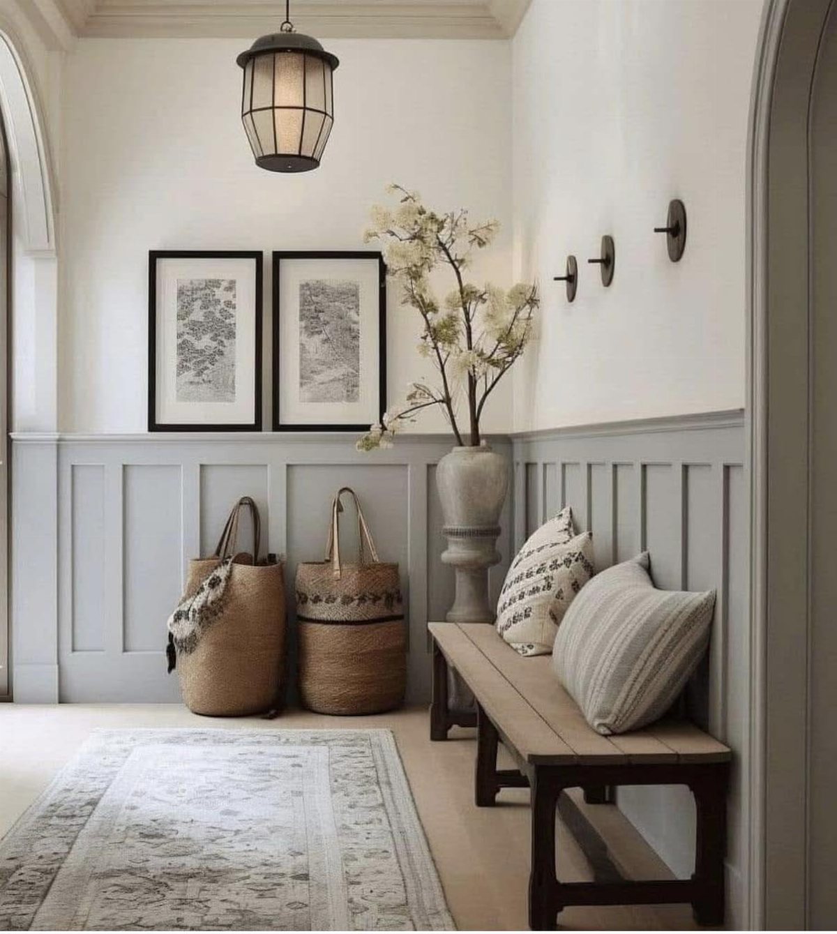 Grey wainscoting paneling in a bright entryway featuring a wooden bench, woven baskets, and framed art.