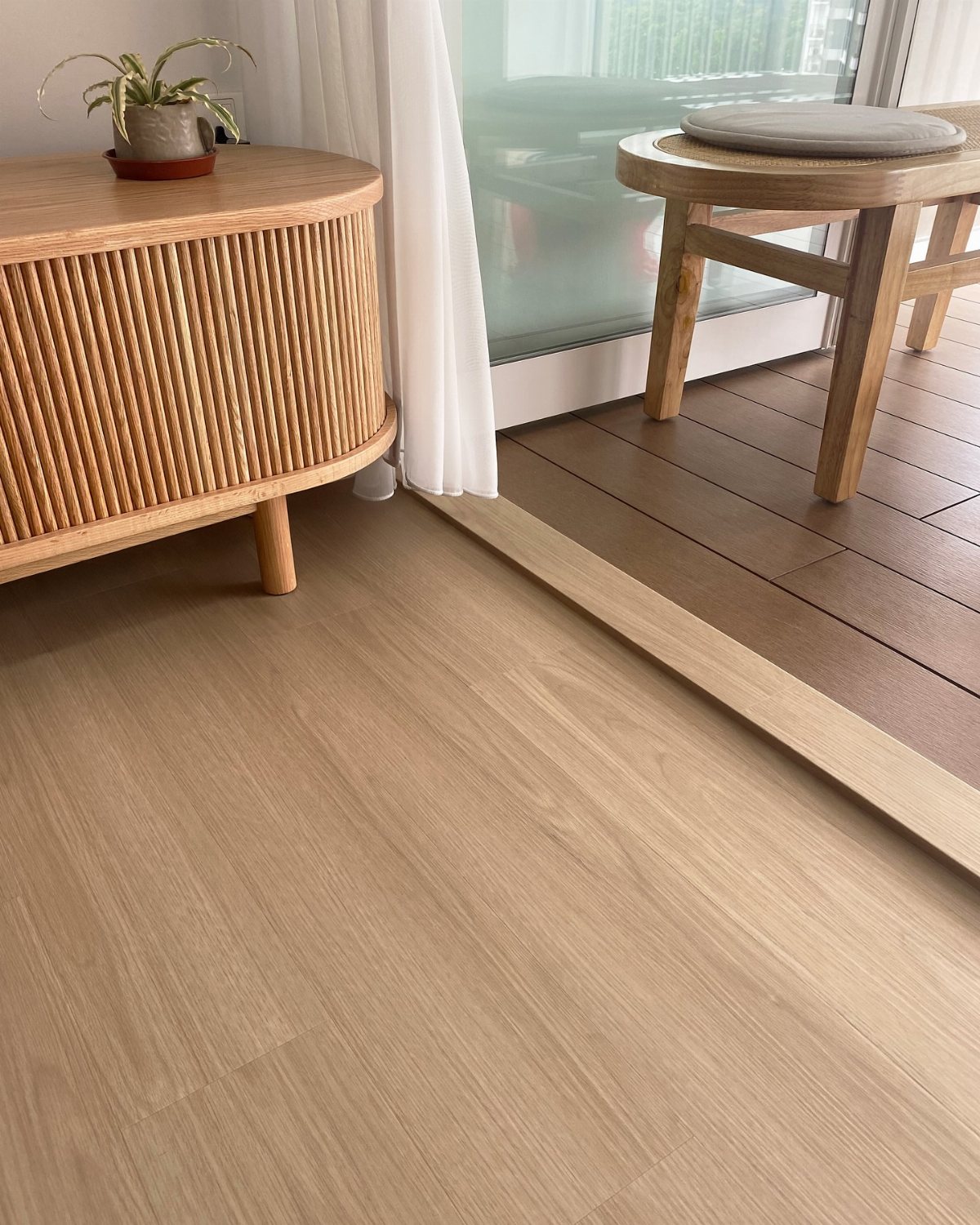 Light natural wood flooring meeting a dark wooden outdoor deck near a wooden sideboard.