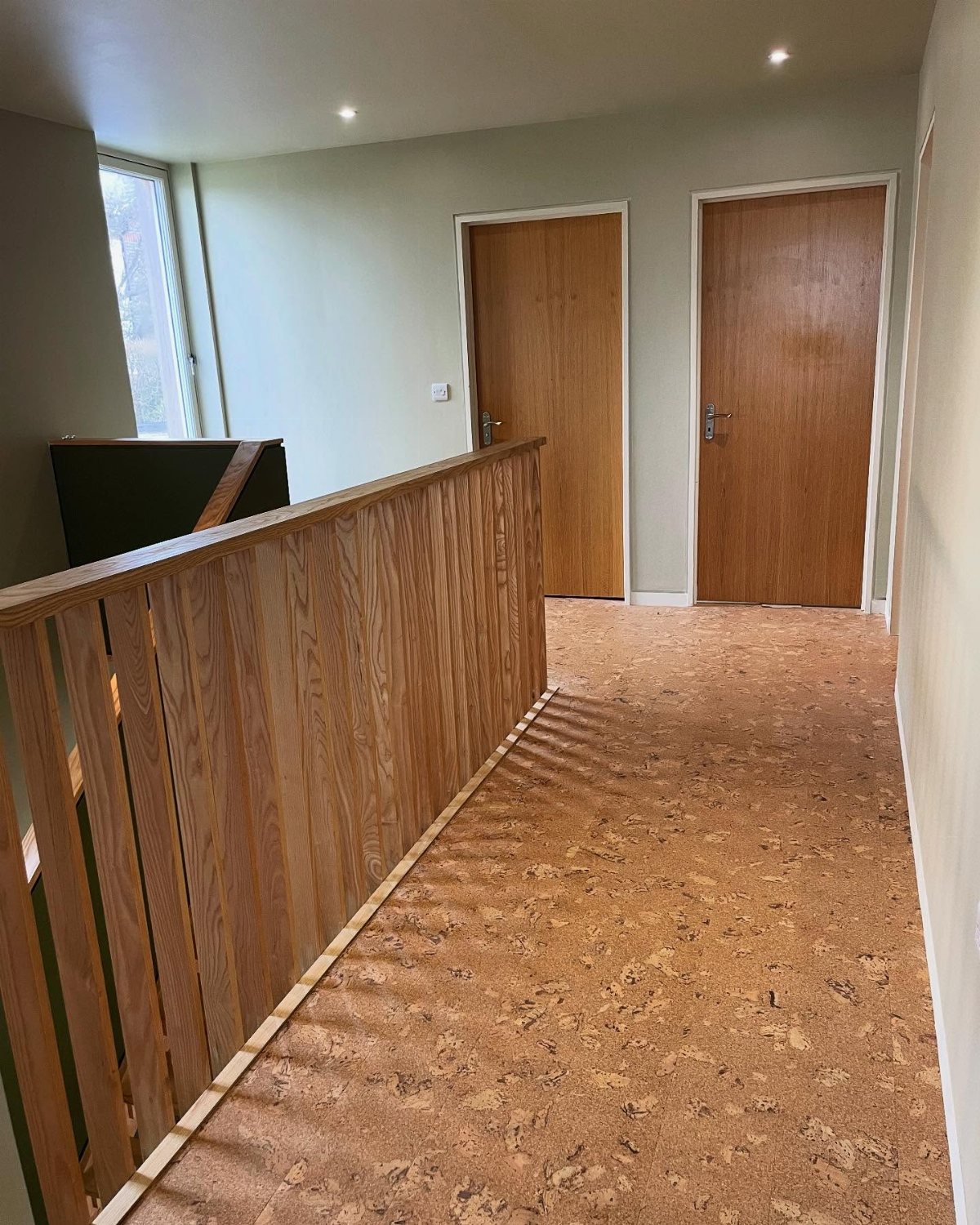 11 Whole House Flooring Ideas That Work from Entry to Bedroom 8 Cork flooring runs through a hallway next to a wooden banister and two doors.