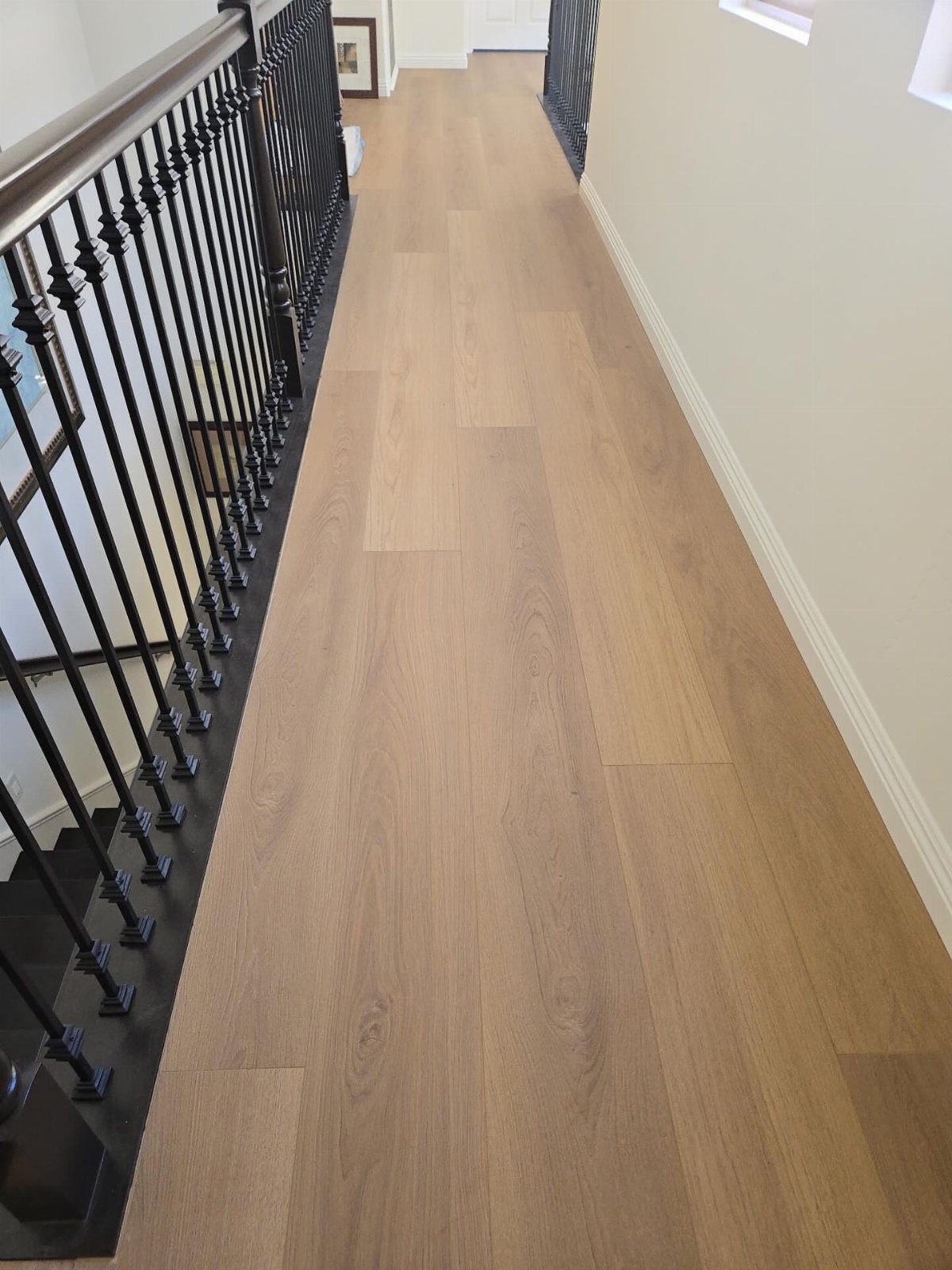 11 Whole House Flooring Ideas That Work from Entry to Bedroom 3 Light brown laminate flooring installed in a hallway next to a black metal staircase railing.
