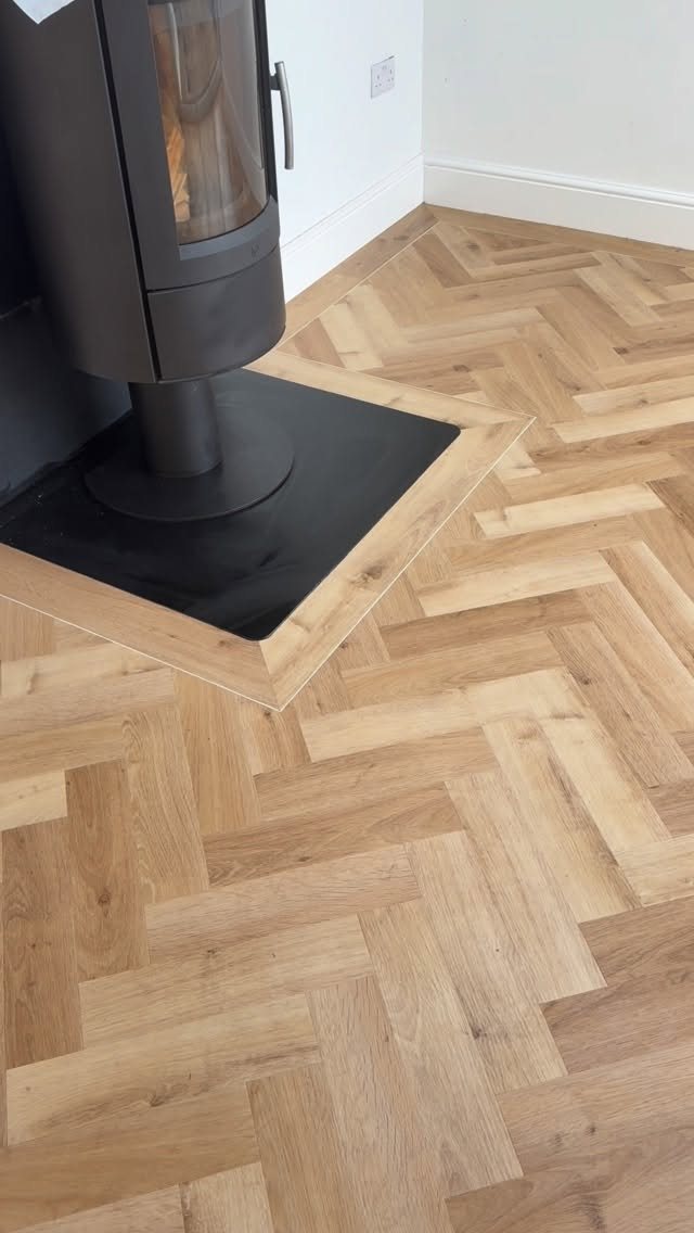 11 Whole House Flooring Ideas That Work from Entry to Bedroom 1 Light wood-effect herringbone flooring installed in a room next to a black wood-burning stove.