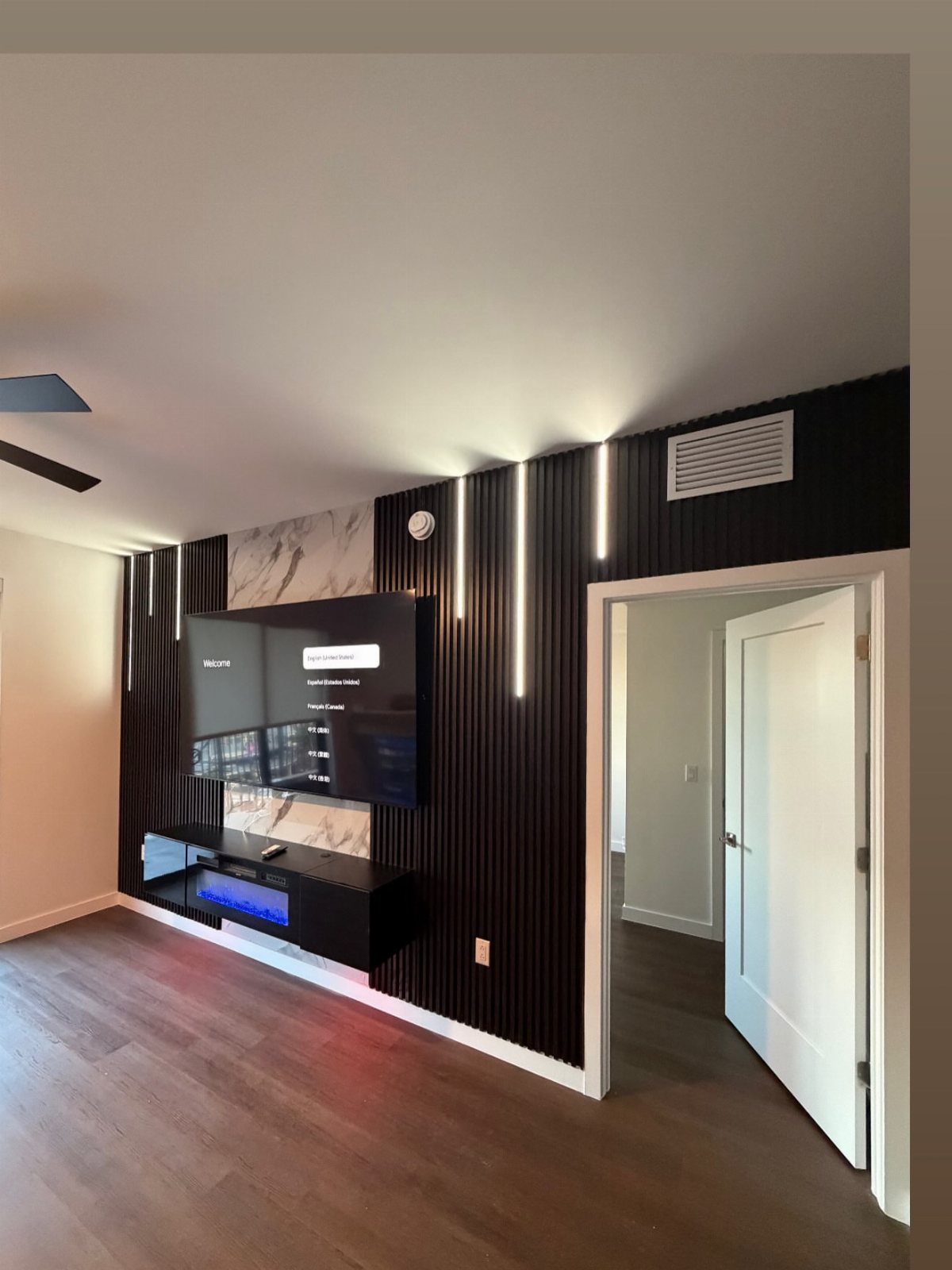 Black vertical wood slat panels on a wall with a mounted television and LED lighting.