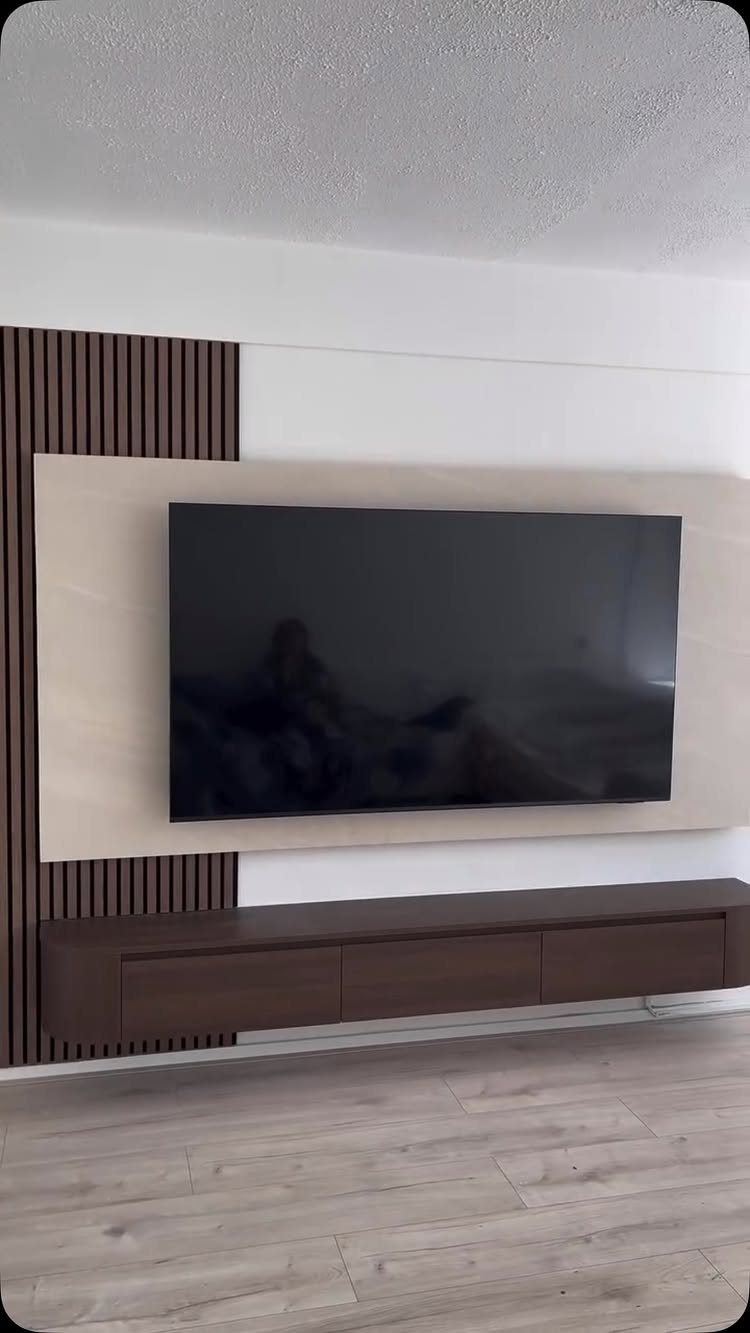 A television mounted on a light wood panel with dark vertical wood slats on the side.